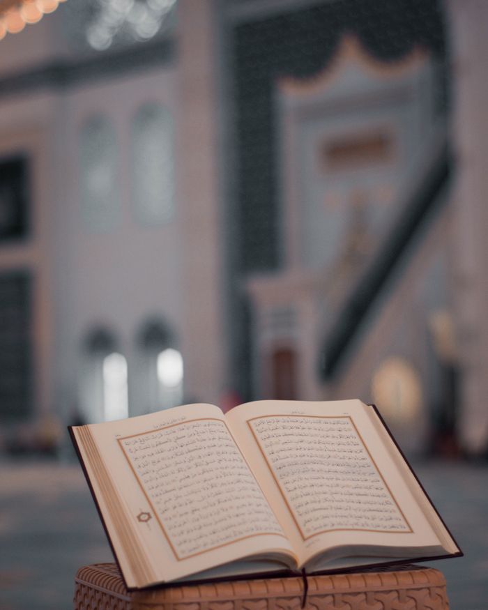 about-us-02 High angle of opened Koran book placed on stone stand in yard of ancient mosque